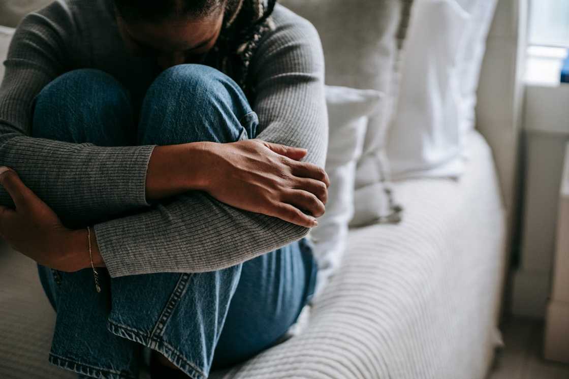 A person sits curled up on a couch, hugging their knees in distress.