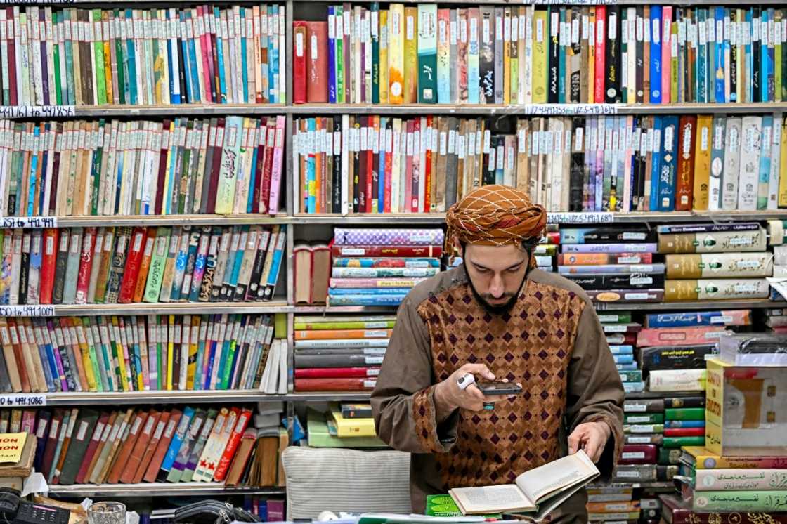 A student takes a photograph of a page of an Urdu book.