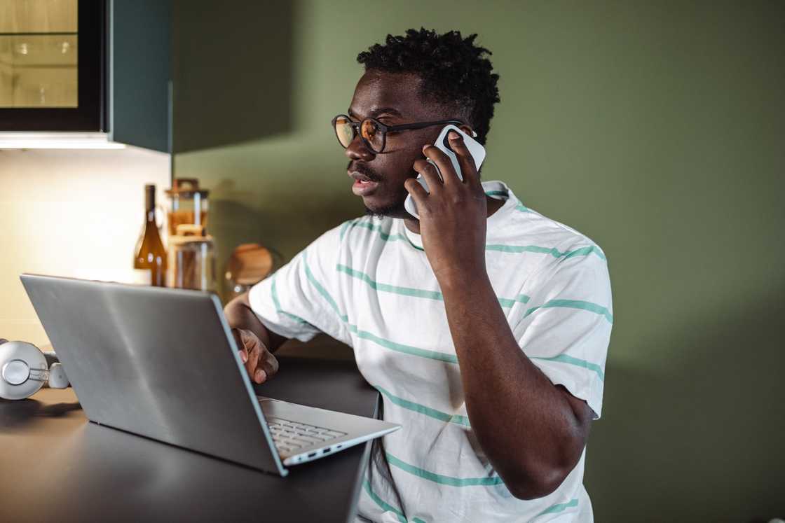 A young man using a laptop and talking on the phone. A young man using a laptop and talking on the phone.