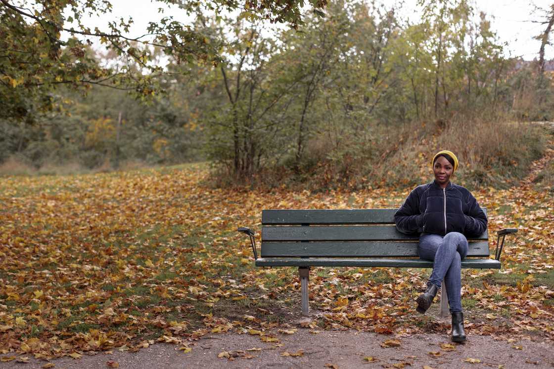Woman sitting on a park bench under autumn trees.
