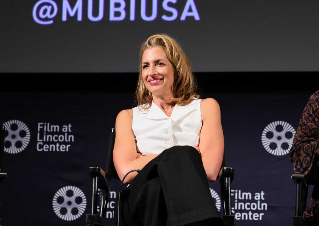 Alysia Reiner smiling in black pants and white sleeveless top