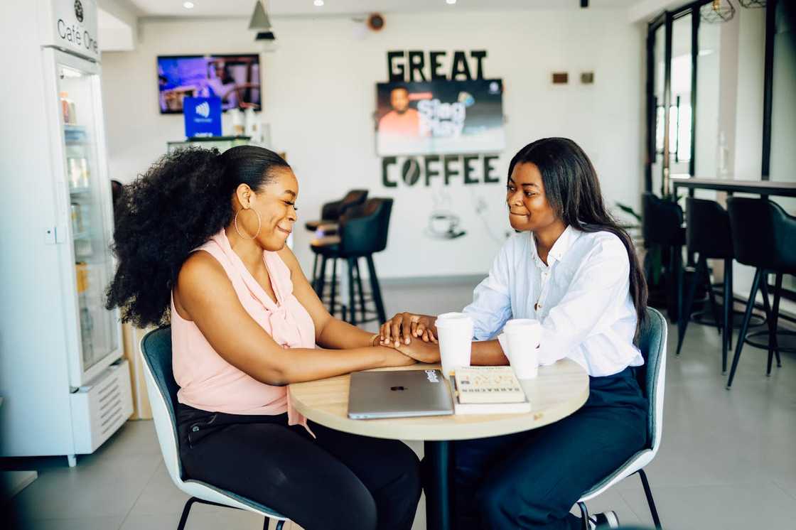 Two women sit at a café table, holding hands and talking over coffee. Two women sit at a café table, holding hands and talking over coffee.