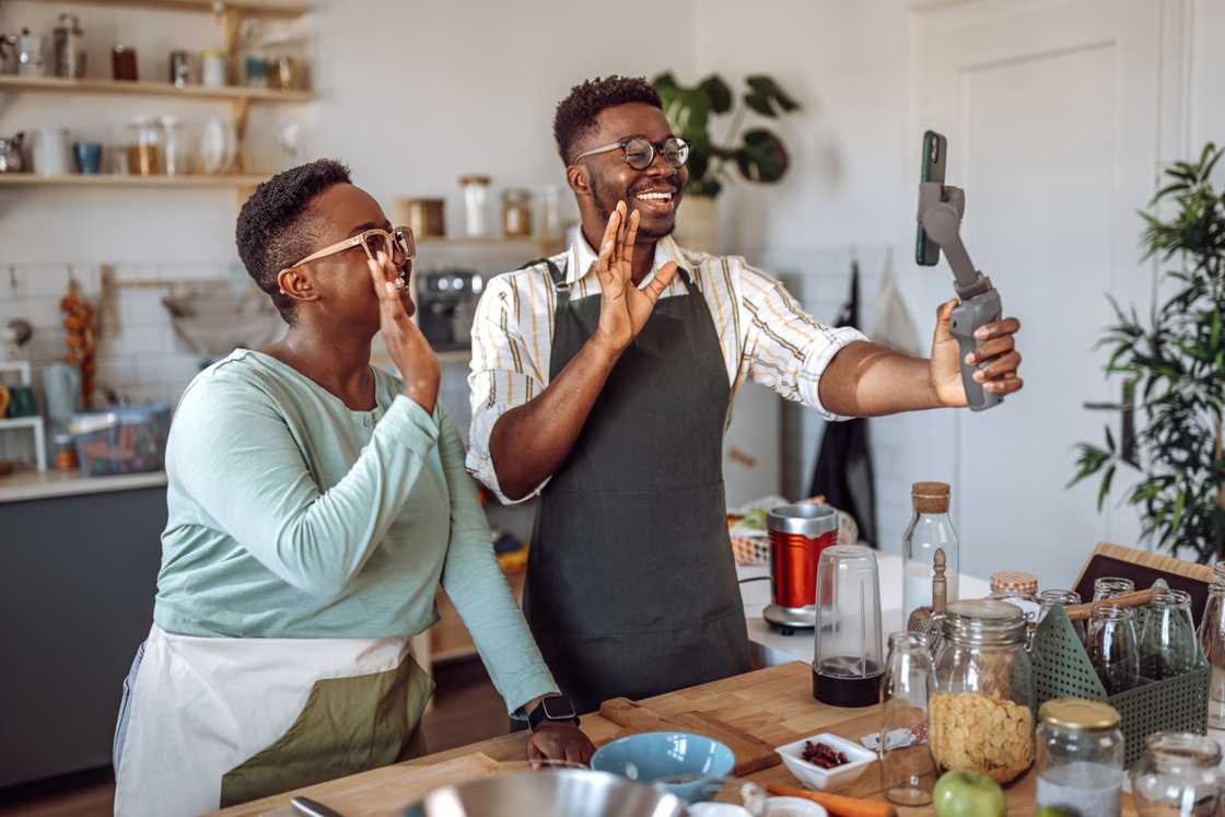 A couple laughs while filming a cooking video in their kitchen. A couple laughs while filming a cooking video in their kitchen.