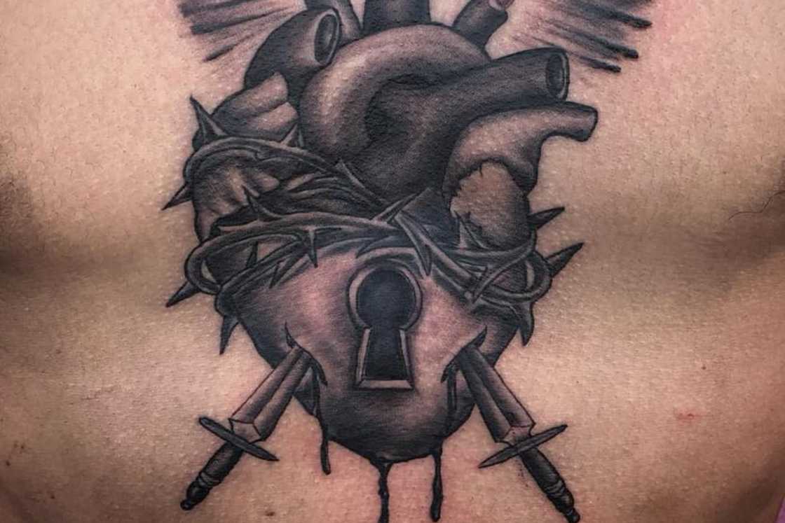 A black sacred heart with daggers and thorns tattoo on the chest A black sacred heart with daggers and thorns tattoo on the chest