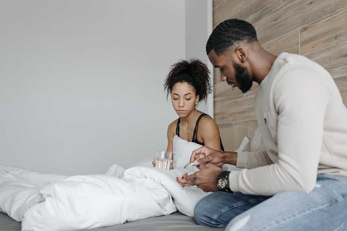 A man helps his unwell partner by preparing medicine while she rests in bed. A man helps his unwell partner by preparing medicine while she rests in bed.