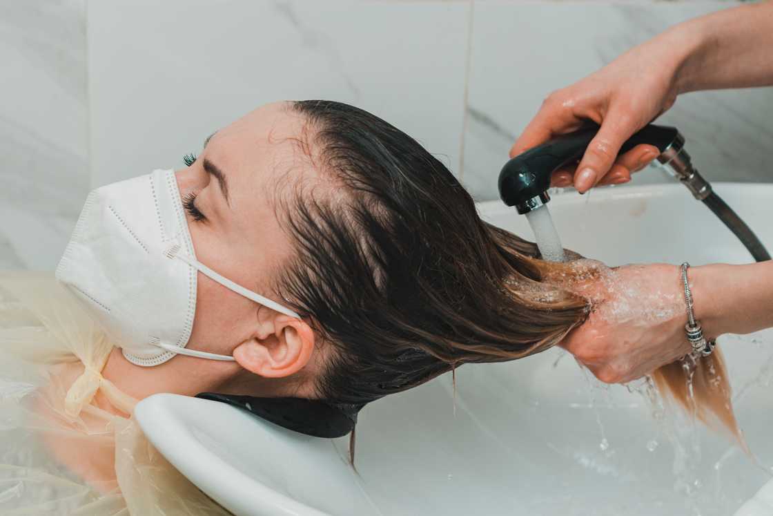 A hairdresser during the world quarantine washes the head in a beauty salon, and a client is wearing a mask