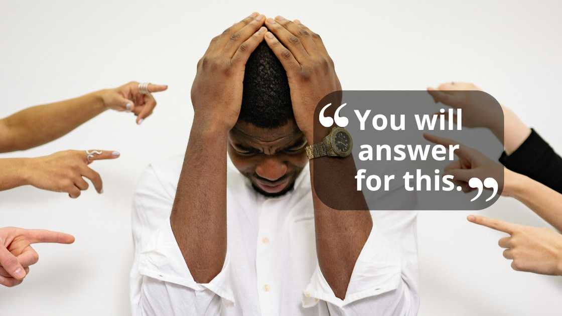 A distressed man clutches his head as multiple hands point at him. A distressed man clutches his head as multiple hands point at him.