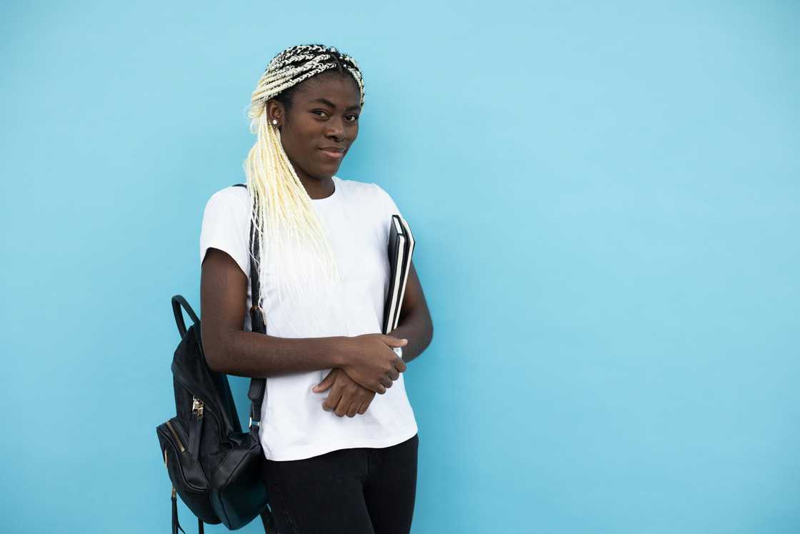 A young lady holding books and carrying a backpack