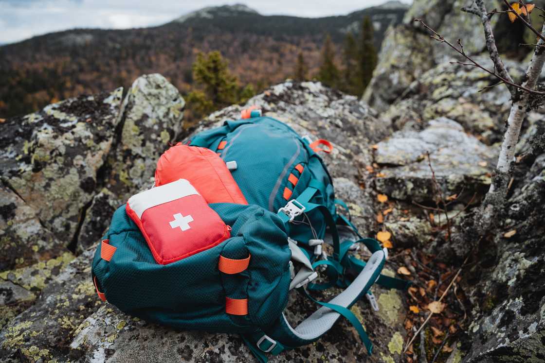A red hiking first aid kit is on a backpack on the mountains. A red hiking first aid kit is on a backpack on the mountains.