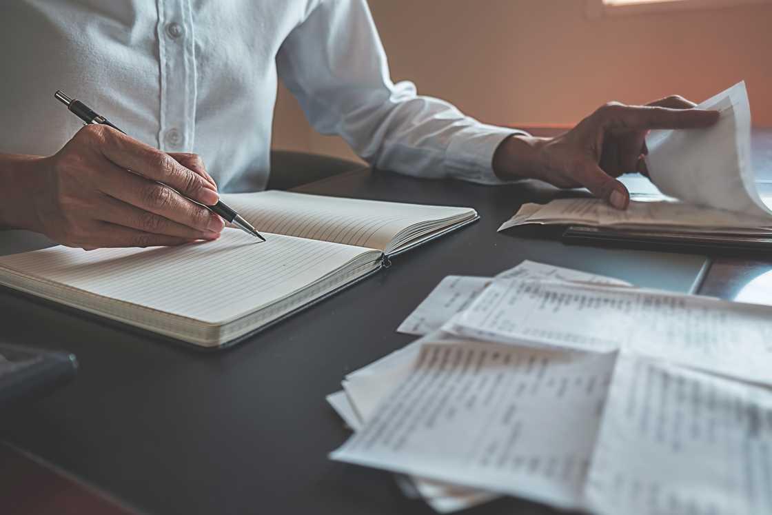 An auditor reviews receipts and a ledger. An auditor reviews receipts and a ledger.