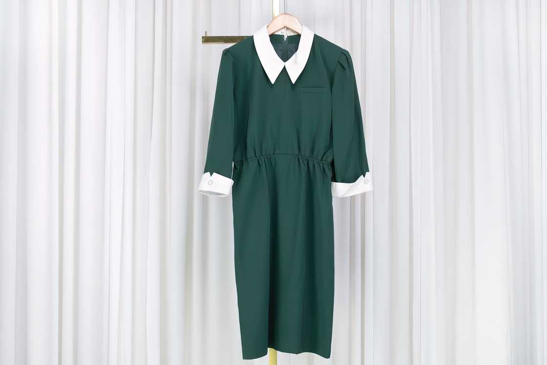 A green dress is hanging from a coat hanger in front of a white curtain A green dress is hanging from a coat hanger in front of a white curtain