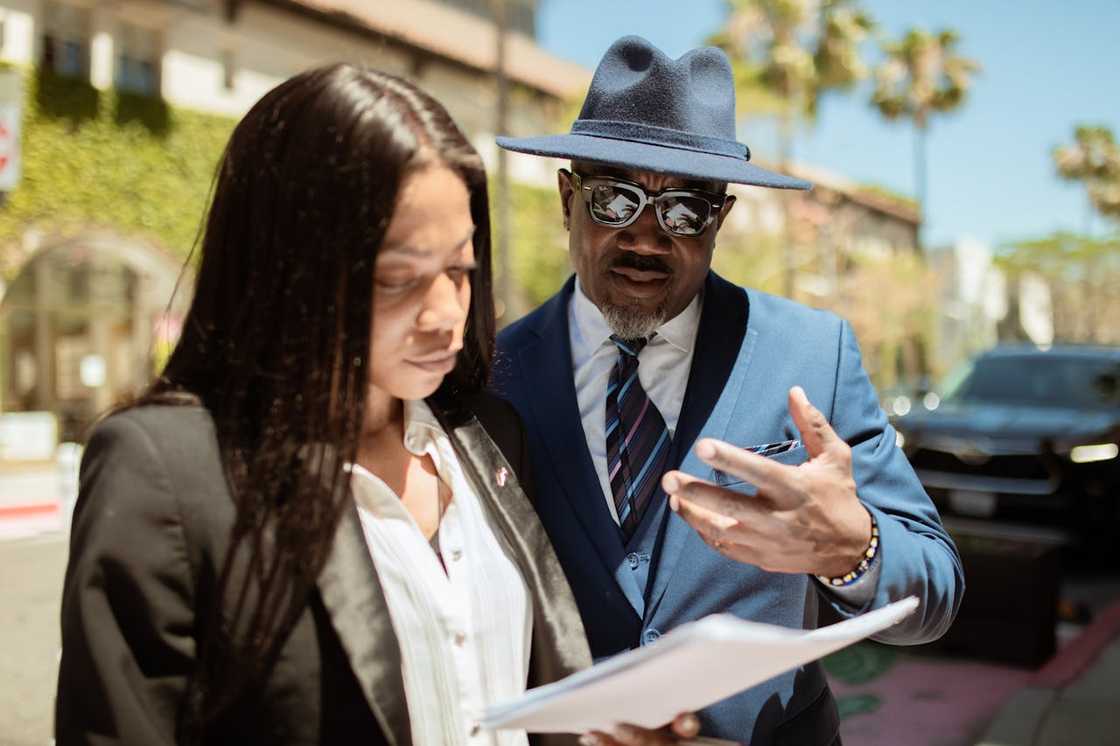 A man and a woman reviewing papers outdoors in business attire.