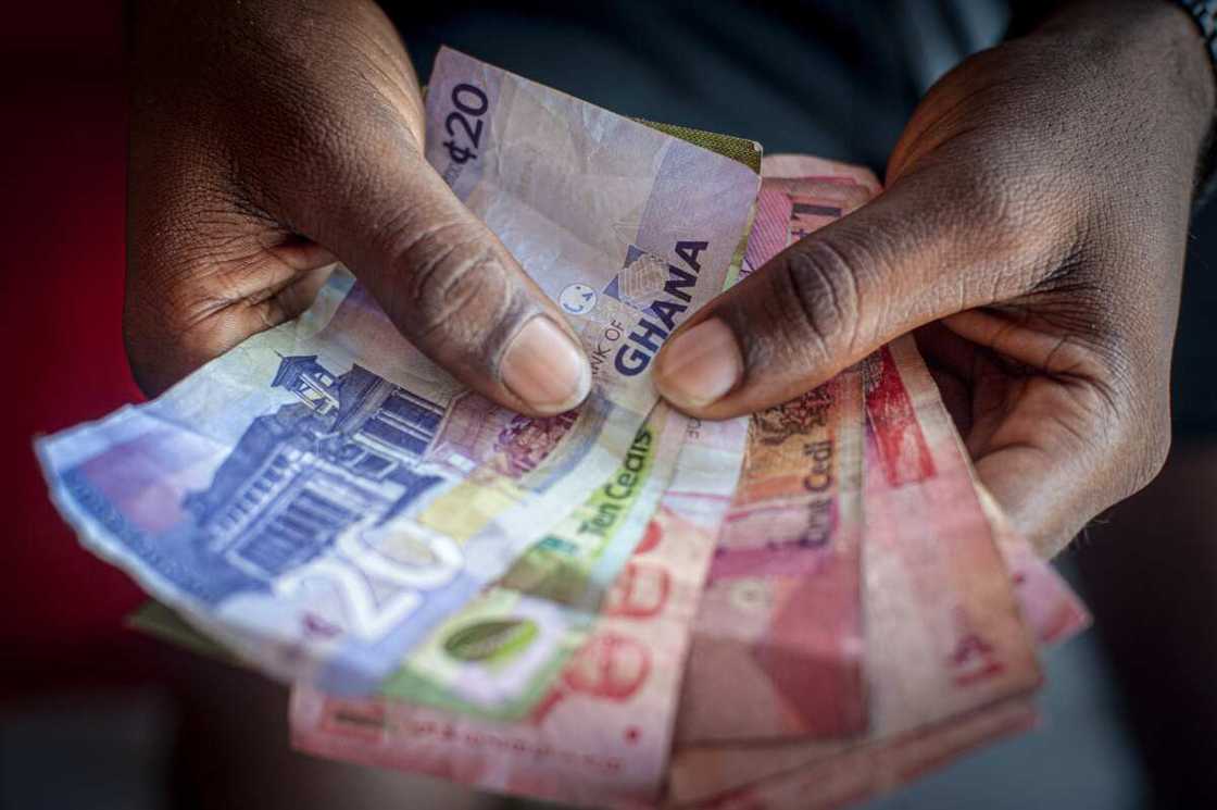 A man holds a bundle of Ghanaian cedi banknotes