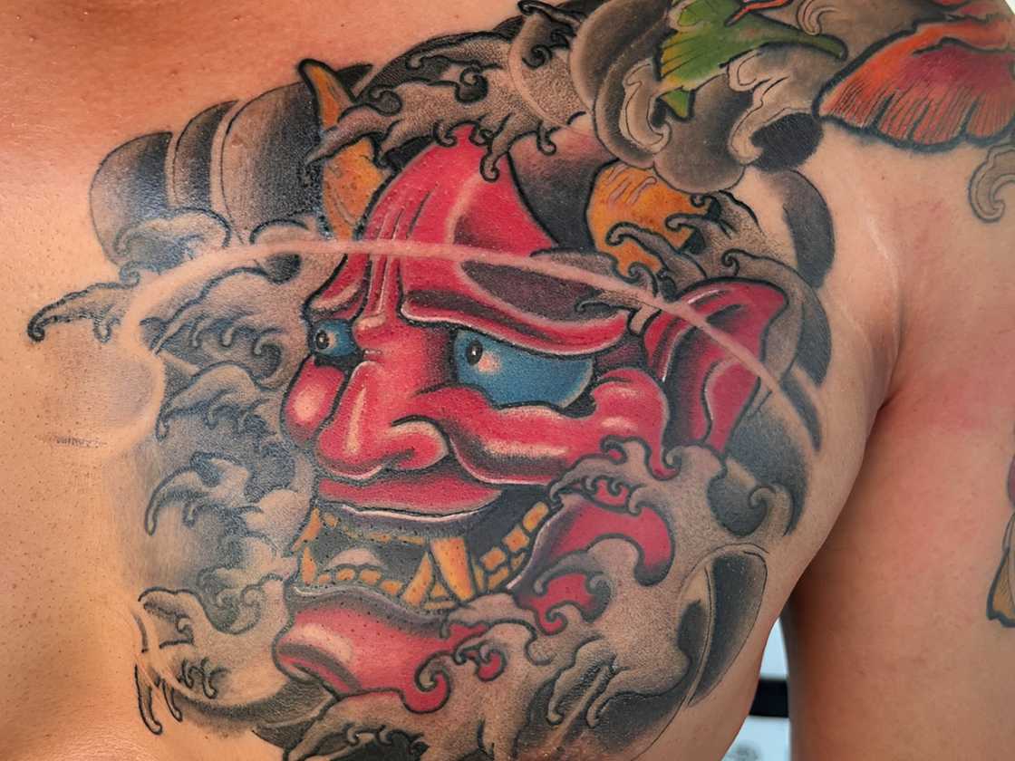 A red oni mask chest tattoo on a cloudy background A red oni mask chest tattoo on a cloudy background