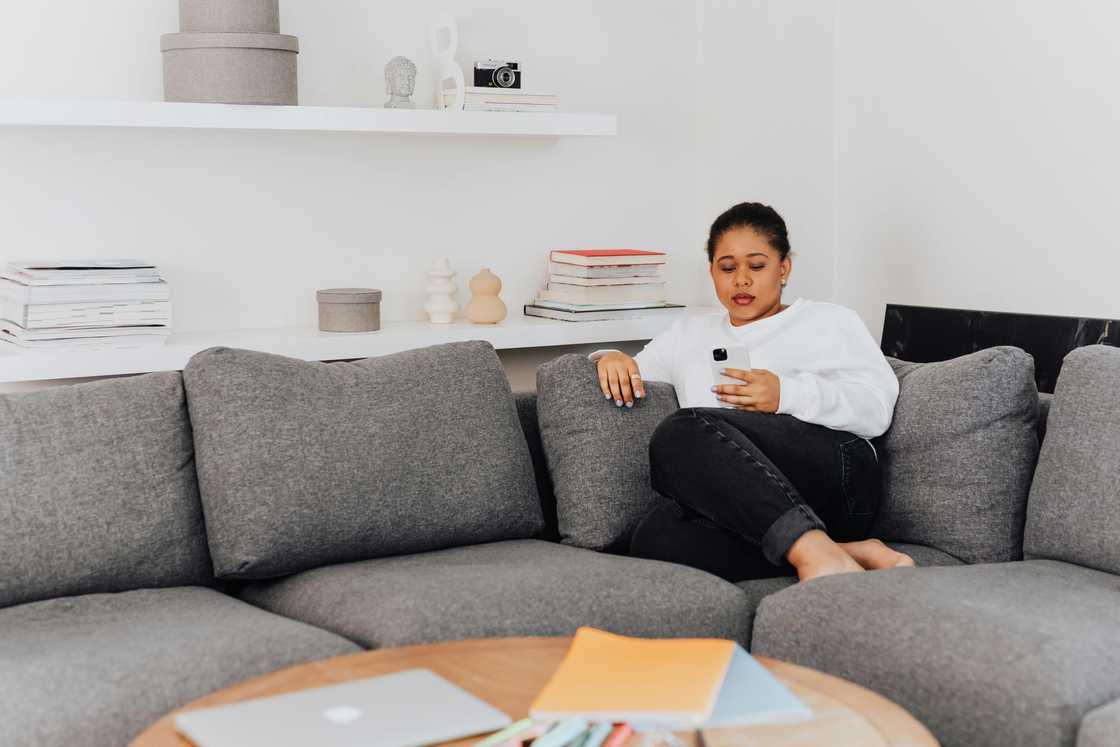 A woman scrolls through a phone while seated on a sofa A woman scrolls through a phone while seated on a sofa