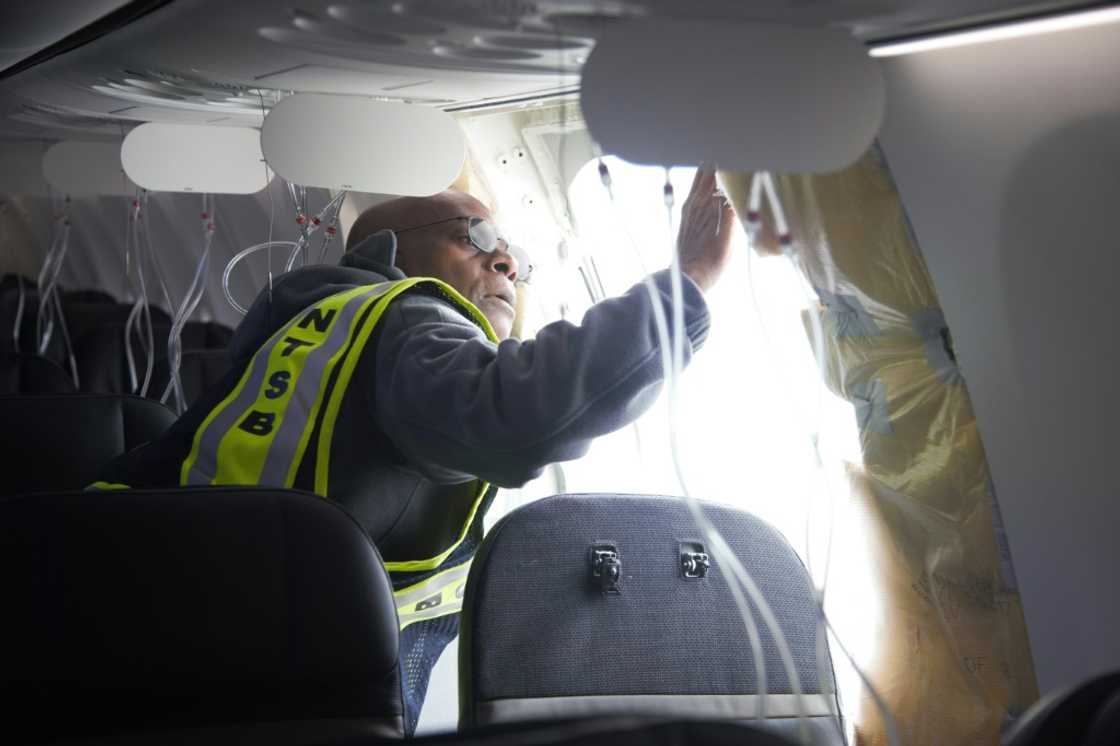A man inspects a hole in the cabin of a Boeing airplane, the result of a fuselage panel blowing off mid-flight A man inspects a hole in the cabin of a Boeing airplane, the result of a fuselage panel blowing off mid-flight