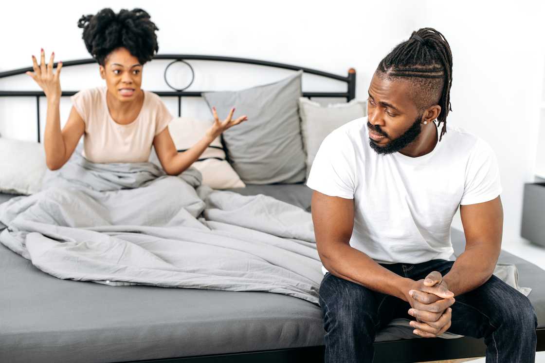 A woman scolds her upset husband sitting on the bed A woman scolds her upset husband sitting on the bed