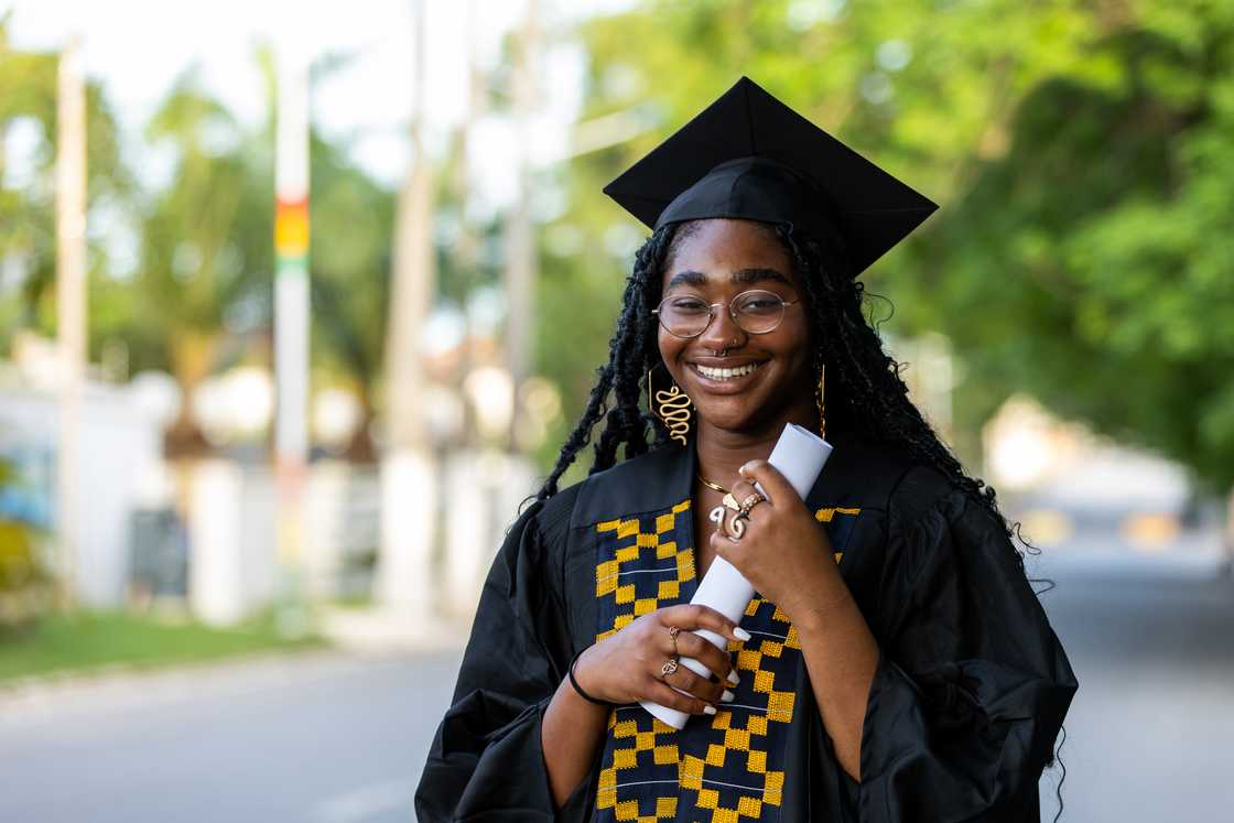 A black female University graduate wearing a black gown and cap, holding her diploma certificate