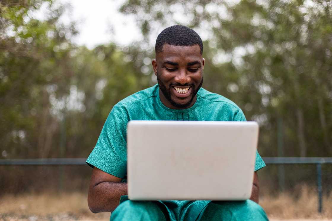 A young African man with a laptop computer outdoors, applying for university admission online