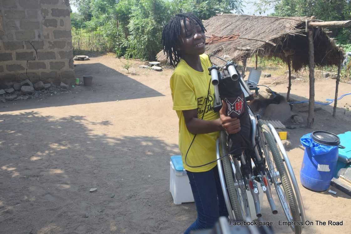 Empress Esi carrying a wheelchair for a physically challenged person.
