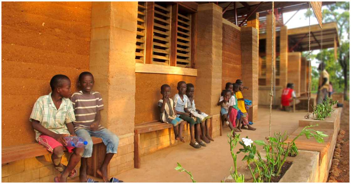 Children sitting infront of the mud cafeteria