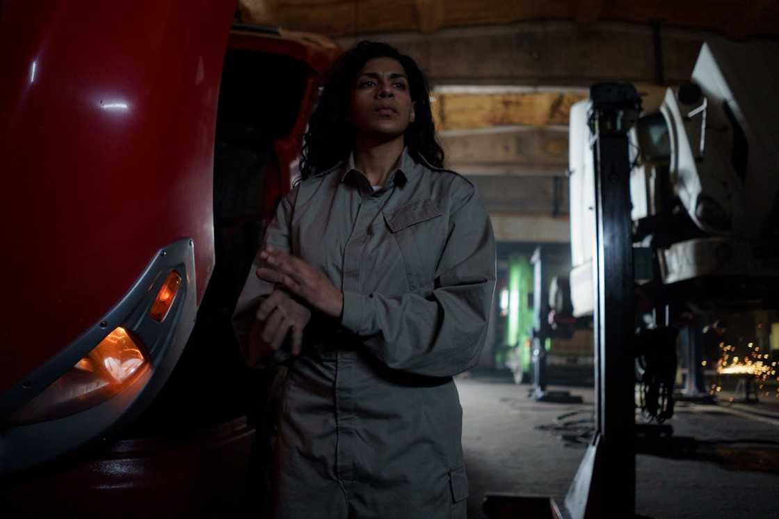 Mechanic standing in a workshop beside a large vehicle. Mechanic standing in a workshop beside a large vehicle.