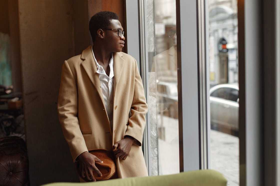 A young man standing alone by a window.