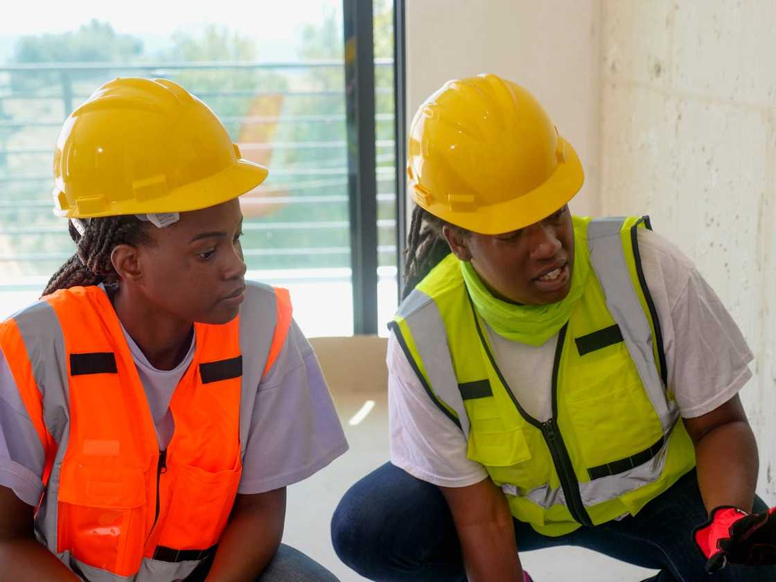 Two construction workers in hard hats discuss work on a building site.