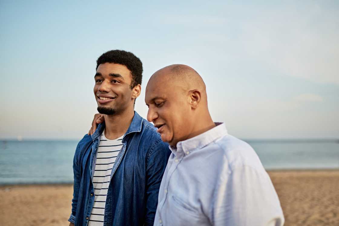 A man in his 20s and his father walk and talk a Beach
