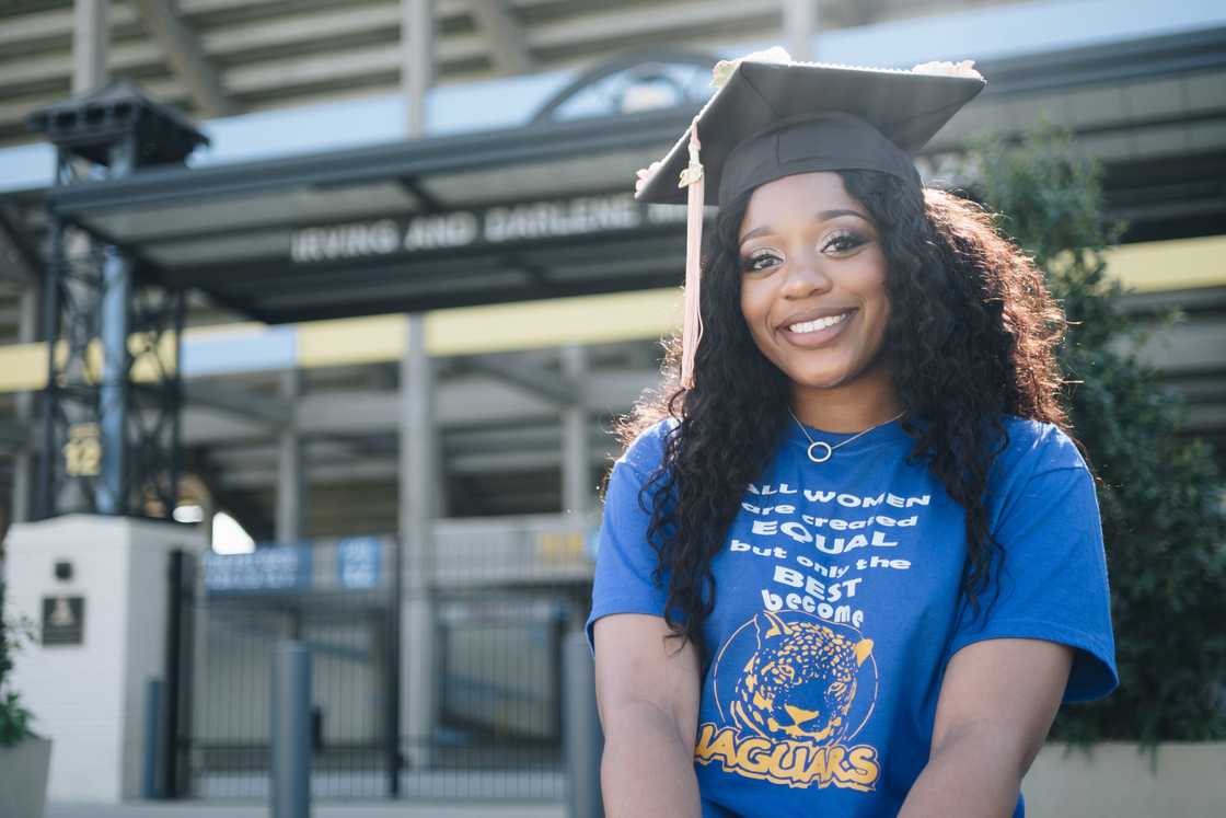 A lady is wearing a black graduation cap and a blue tee with writings A lady is wearing a black graduation cap and a blue tee with writings