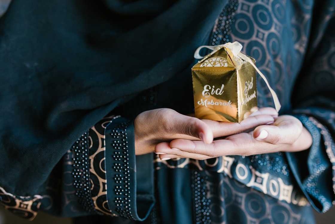 A person holds a beautifully wrapped "Eid Mubarak" gift.