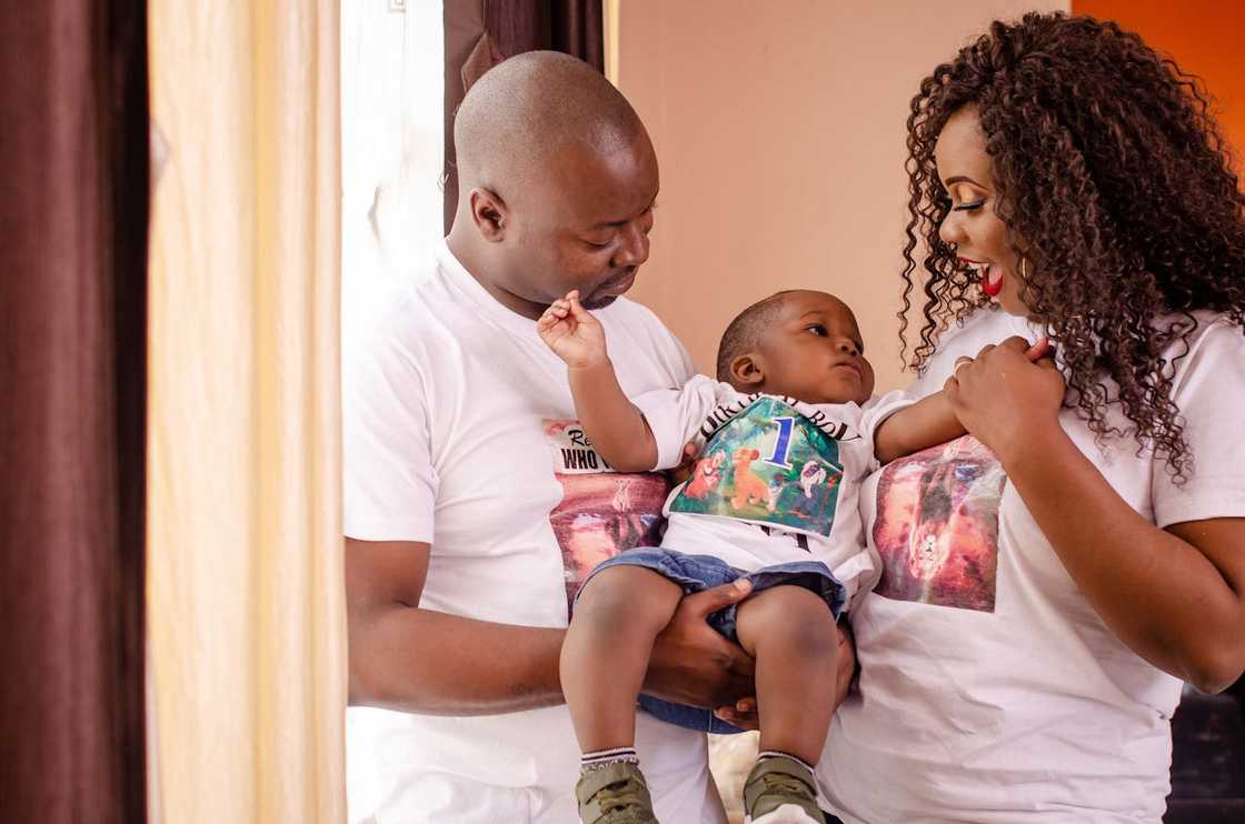 Smiling parents hold their baby indoors.