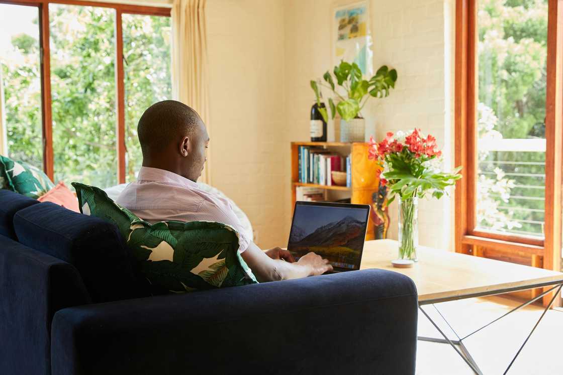 A man studying on a laptop while sitting on a navy blue couch A man studying on a laptop while sitting on a navy blue couch
