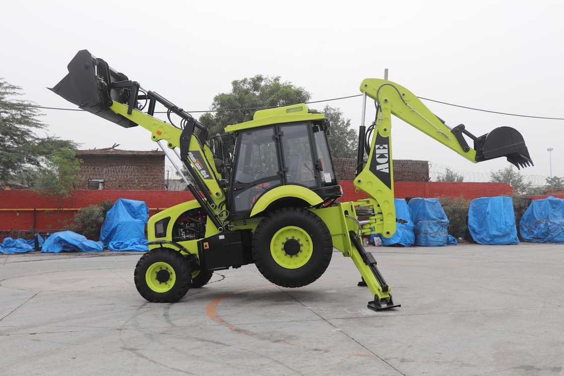 A green backhoe loader stands parked at a work yard.
