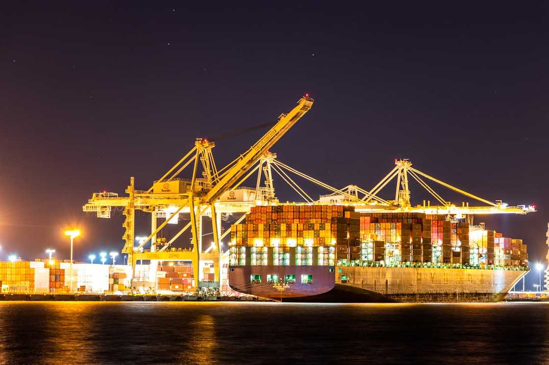 A container ship docked at a brightly lit port at night. A container ship docked at a brightly lit port at night.