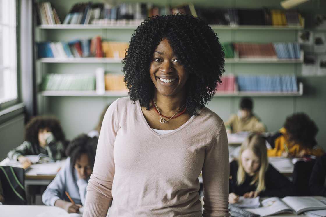 A teacher with curly hair standing in a classroom A teacher with curly hair standing in a classroom