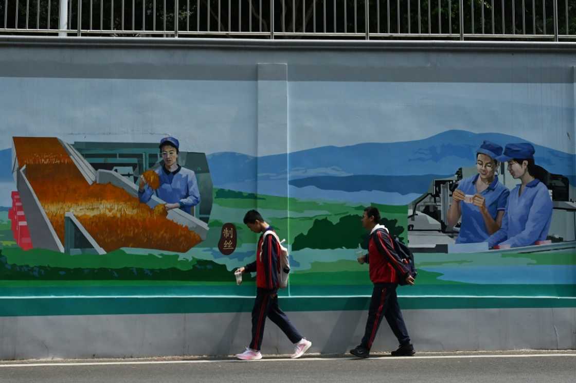 Students walk past a mural of workers at a cigarette factory in Yuxi, China Students walk past a mural of workers at a cigarette factory in Yuxi, China