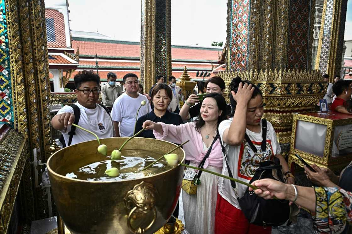 Chinese tourists dipping lotus bulbs in a water bowl, at the Grand Palace in Bangkok Chinese tourists dipping lotus bulbs in a water bowl, at the Grand Palace in Bangkok