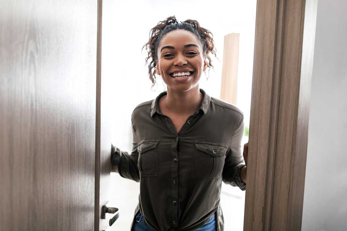 Cheerful young woman opening door and smiling
