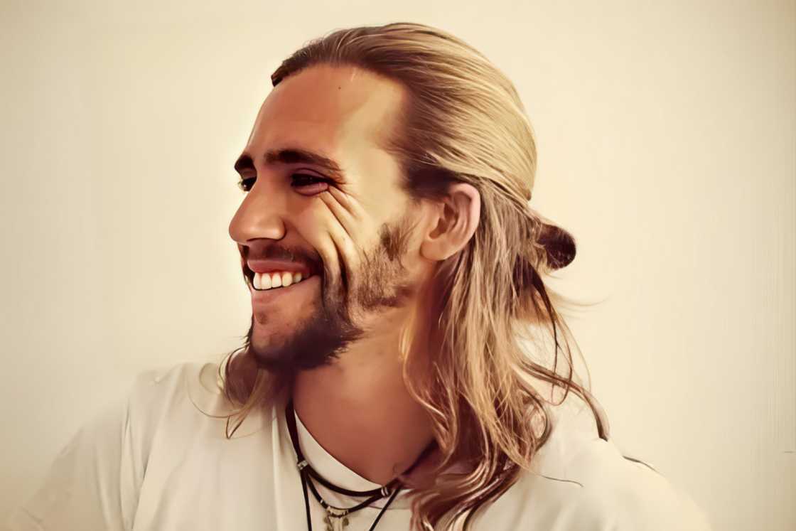 A man with a half-up semi-bun style smiles for a photo A man with a half-up semi-bun style smiles for a photo