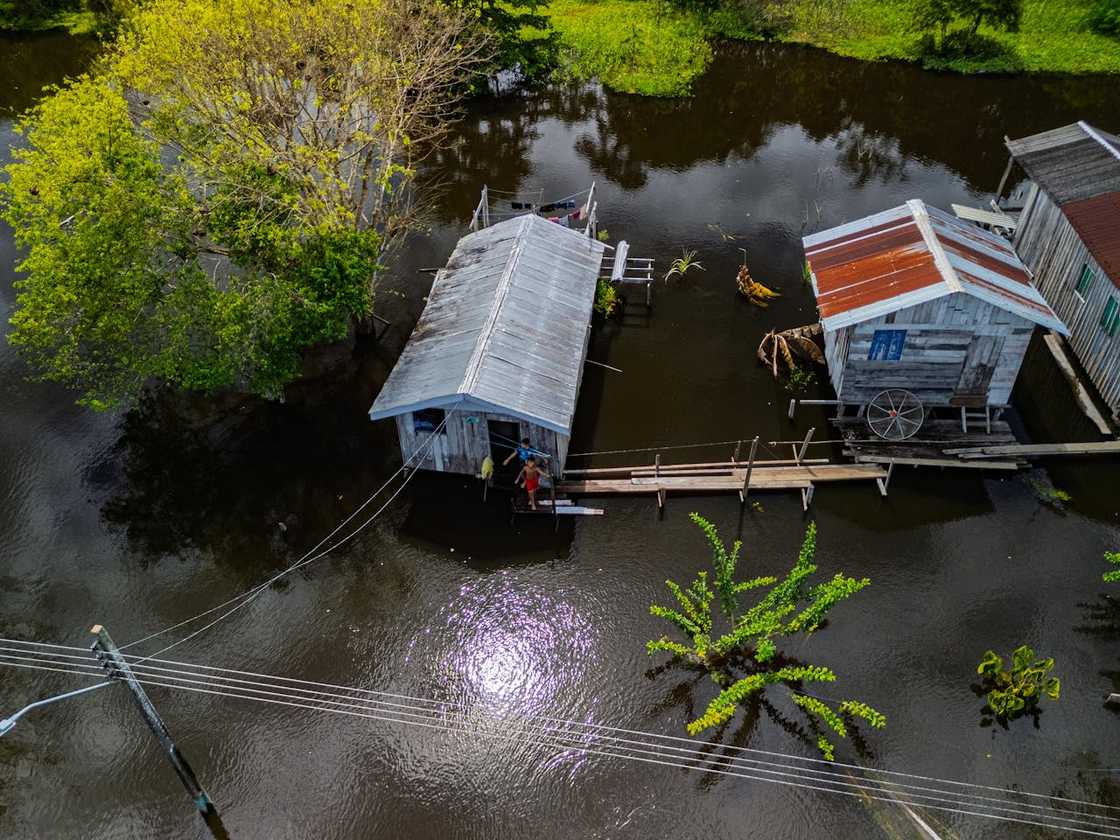 Flooded wooden houses stand along a river connected by a walkway.