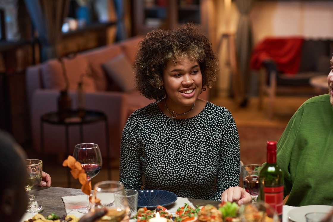 Friends laughing around a restaurant dinner table while one woman sits quietly.