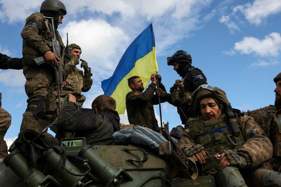 Ukrainian soldiers fix a national flag atop an armoured personnel carrier near Lyman in the Donetsk region