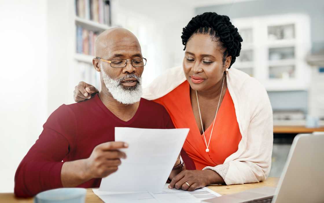 Two adults sit in a home setting, reviewing a piece of paper together.