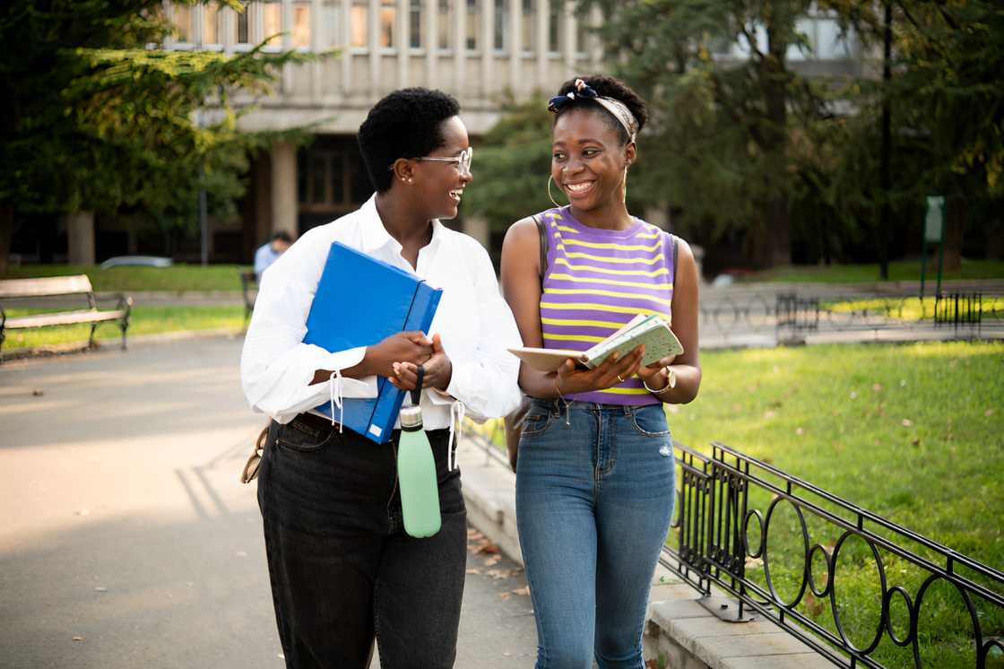 Two female African-American students discussing their lessons while going to the college class