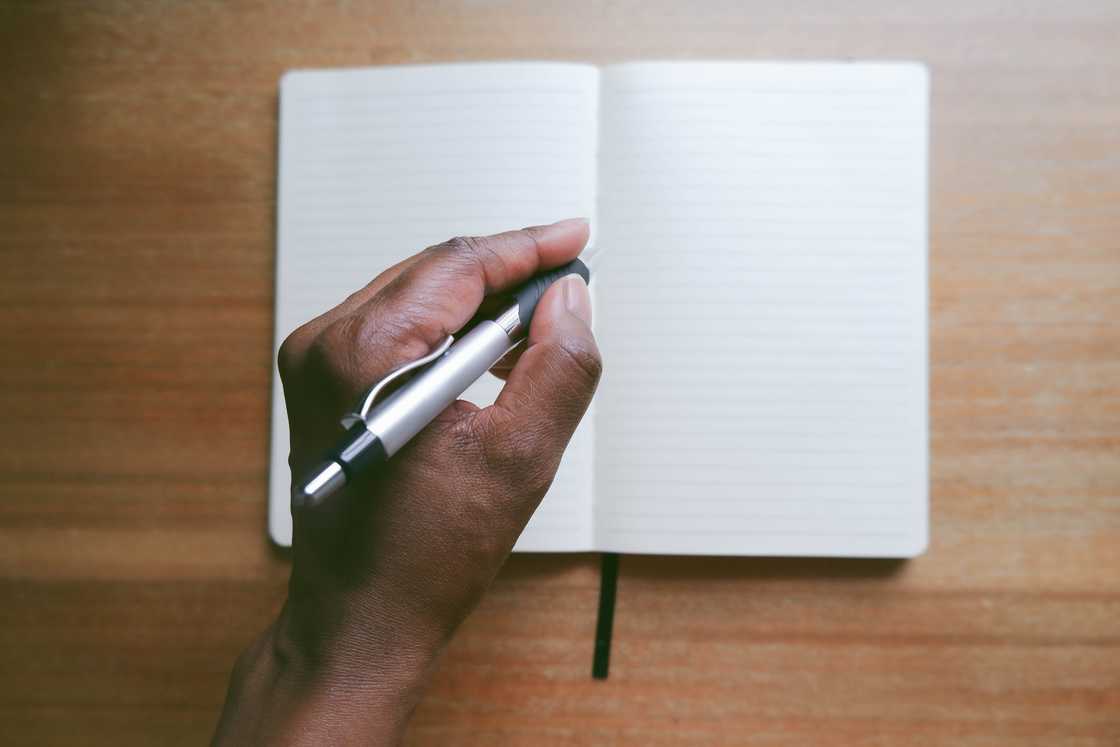 Hand holds pen above a blank notebook on a wooden surface. Hand holds pen above a blank notebook on a wooden surface.