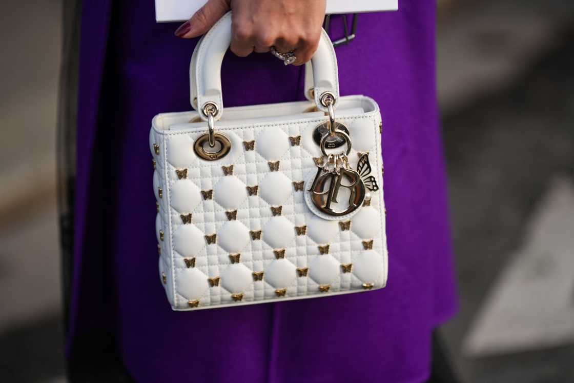 A woman in a purple dress holding a white and golden Dior Lady Dior bag. A woman in a purple dress holding a white and golden Dior Lady Dior bag.