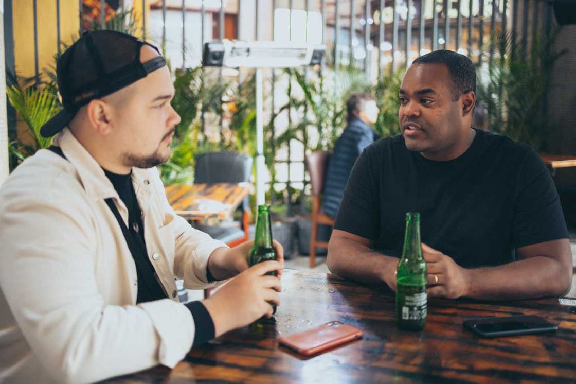 Two friends sit at a small café talking.