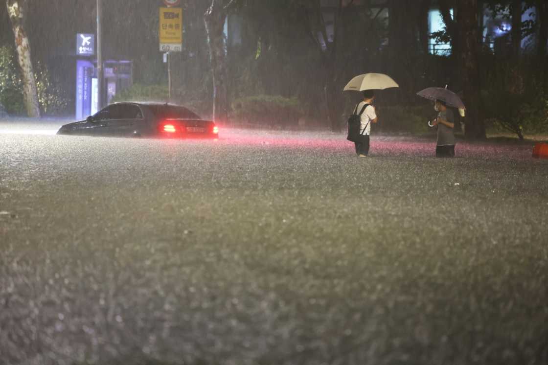 People wade alongside submerged cars during heavy rainfall in Seoul's Gangnam district Monday