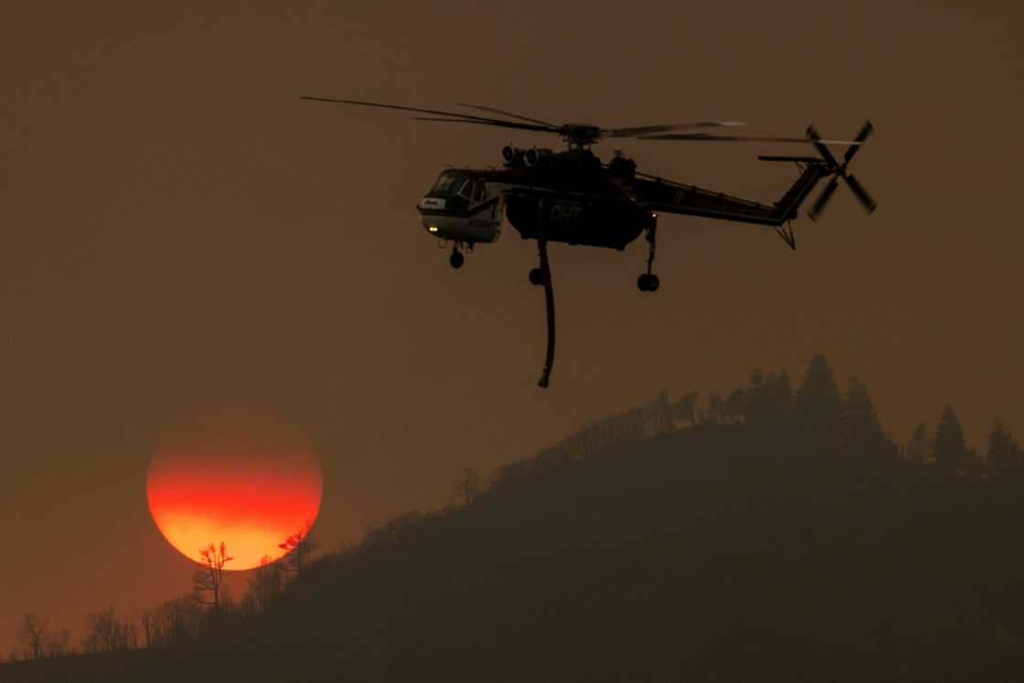 A firefighting helicopter passes the setting sun while fighting the Oak Fire near Mariposa, California